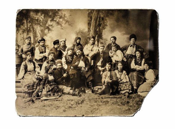 Актори трупи Марка Кропивницького (сидить посередині) сфотографувалися на сцені після вистави. Праворуч від керівника колективу – Микола Садовський, ліворуч – Марія Заньковецька. Зображають сцену ворожіння